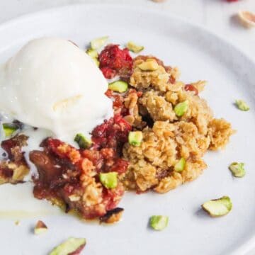 A serving of fruit crumble topped with vanilla ice cream and chopped pistachios on a white plate.