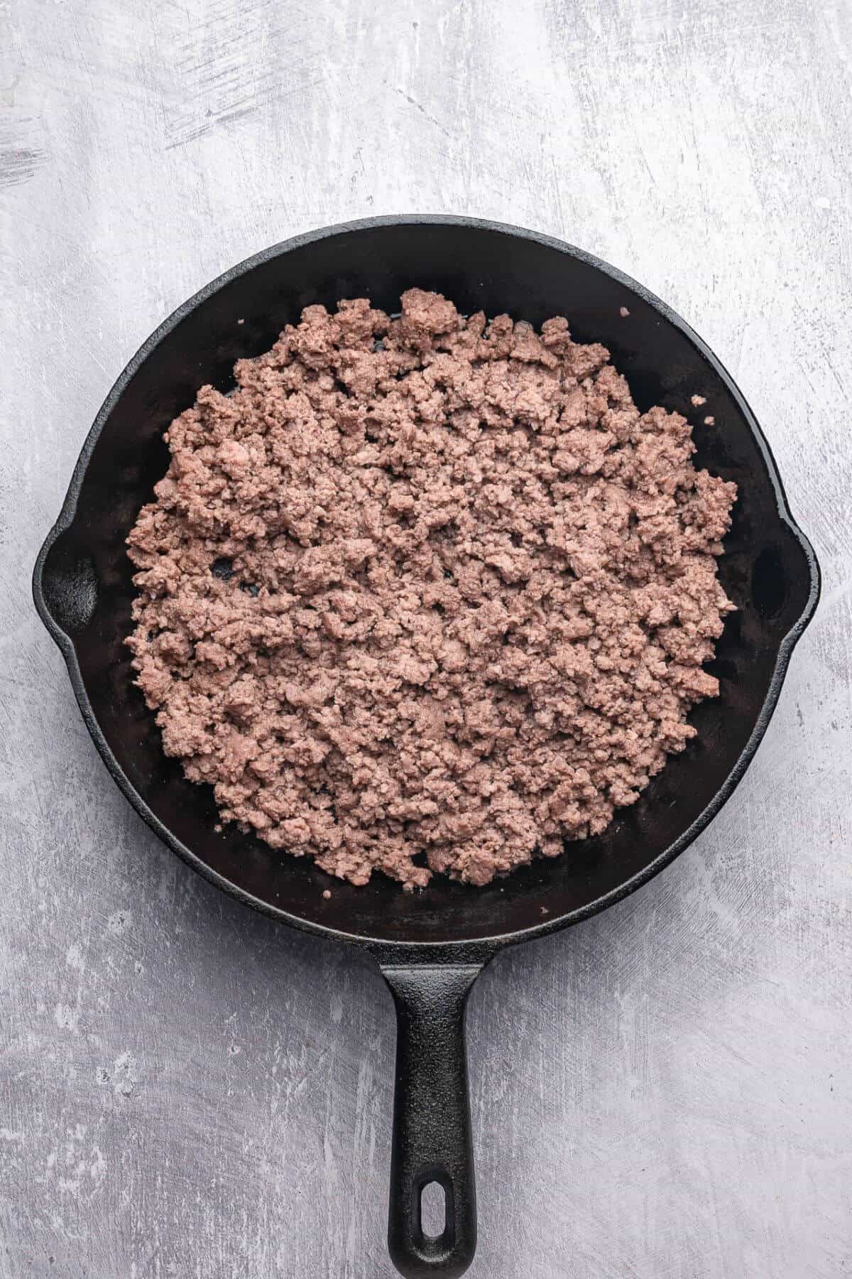 Cooked ground beef in a black cast iron skillet on a light gray textured surface.