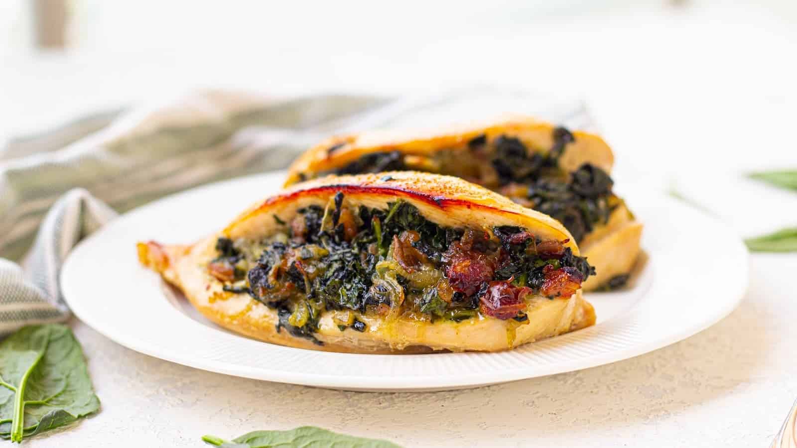 A white plate with two pieces of chicken breast stuffed with spinach, sun-dried tomatoes, and other vegetables.