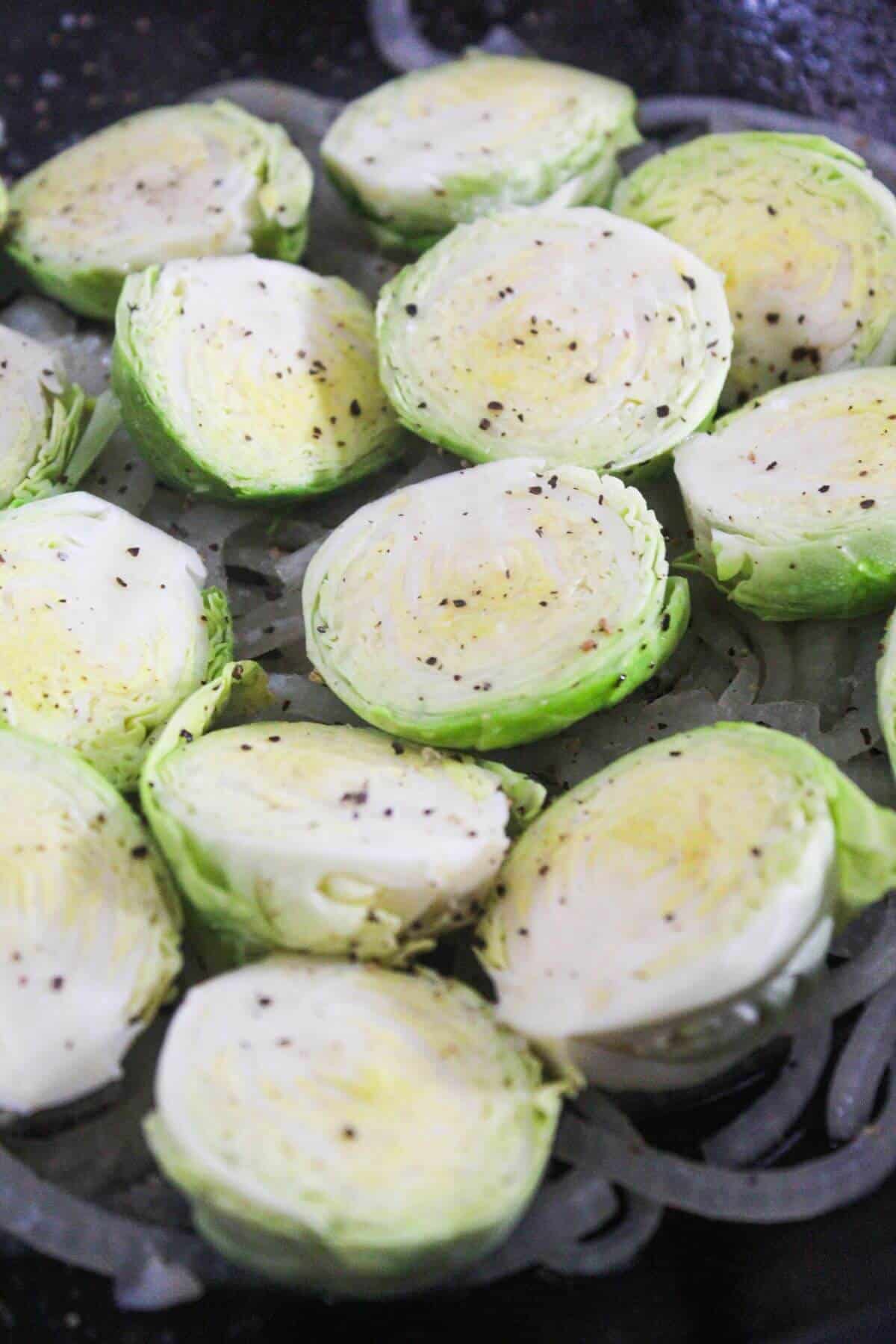 Halved Brussels sprouts arranged in a pan, seasoned with salt and pepper, ready to be cooked.