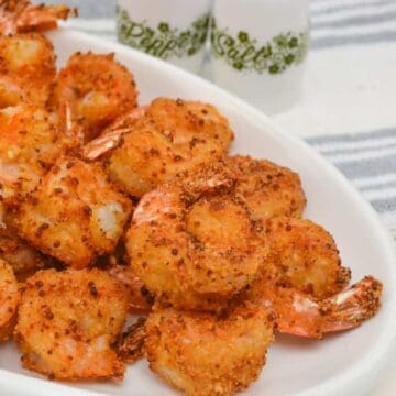 A white plate with several pieces of breaded and seasoned shrimp, with salt and pepper shakers and a striped towel in the background.