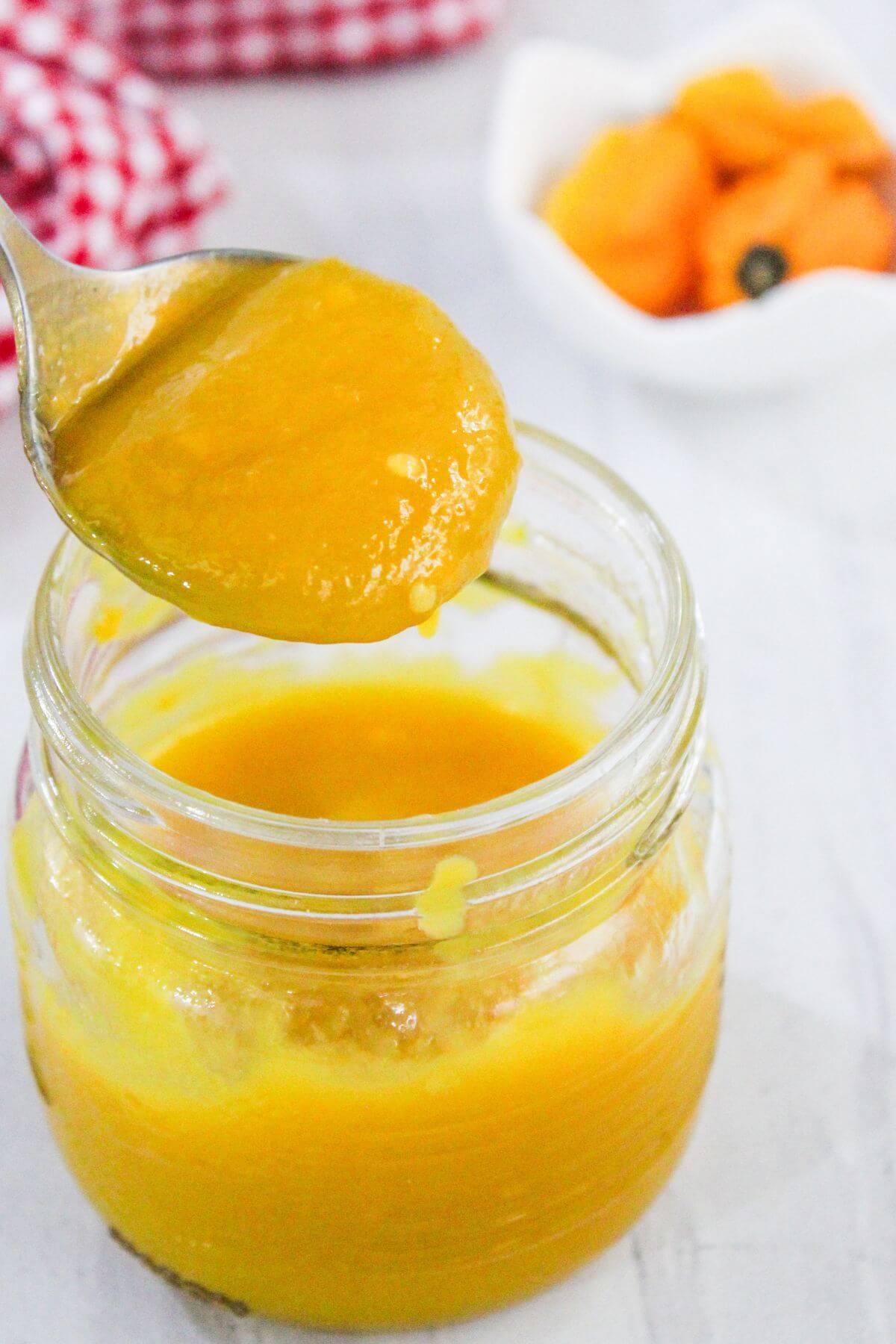 A spoon holds thick orange-yellow puree above an open glass jar, with dried fruit in a small white dish in the background.