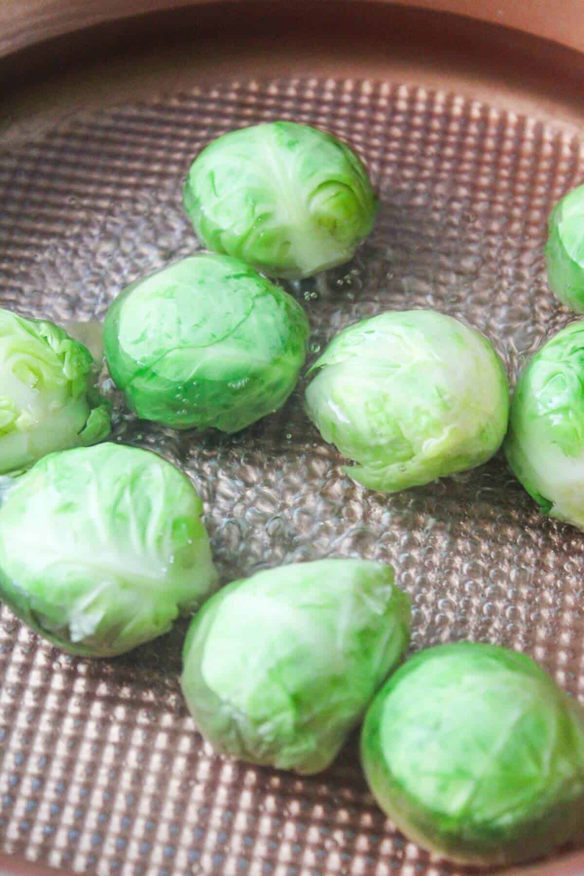 Several Brussels sprouts are being boiled in a copper saucepan filled with water.