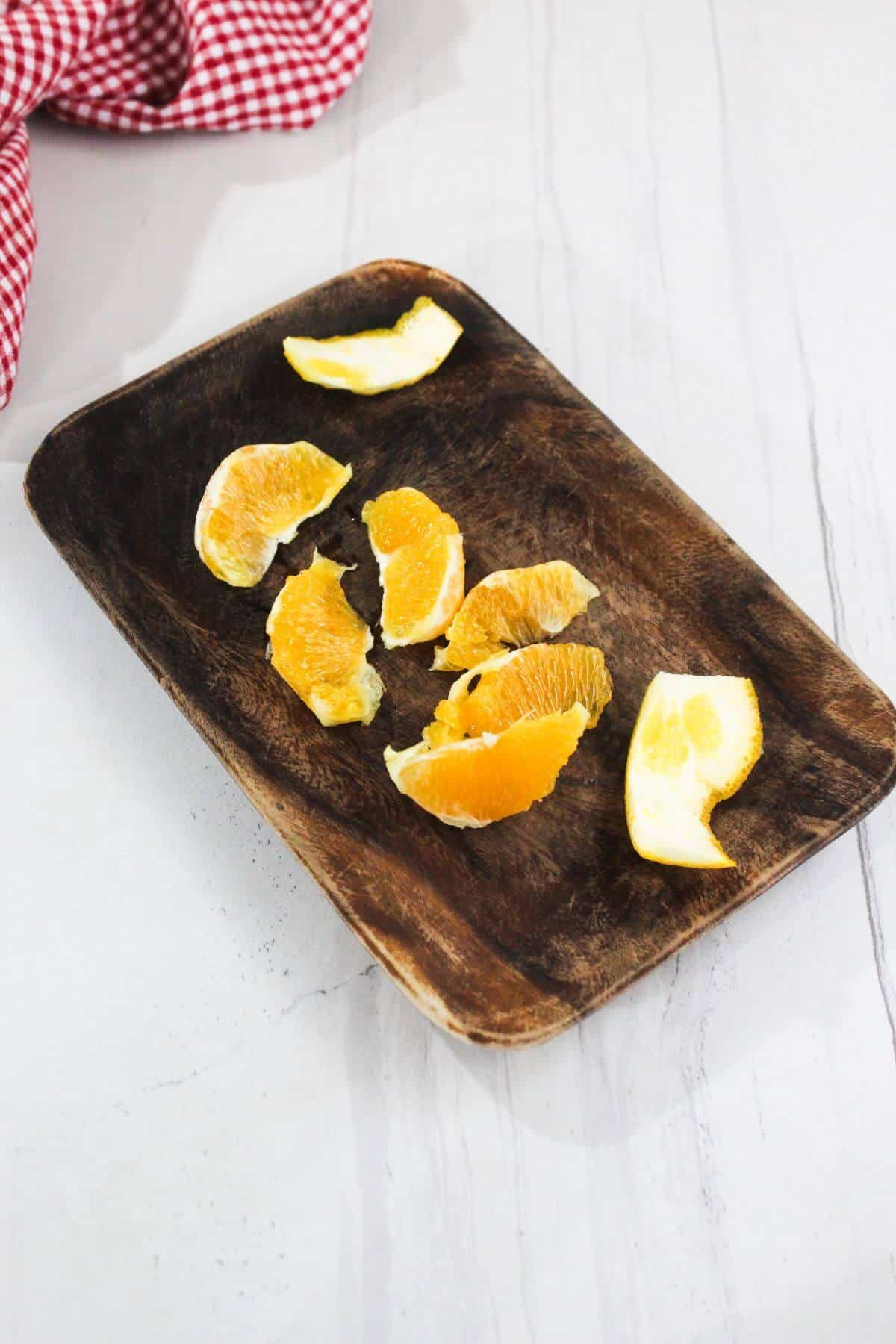 Several orange slices arranged on a rectangular wooden tray, with a red and white checkered cloth partially visible in the background.