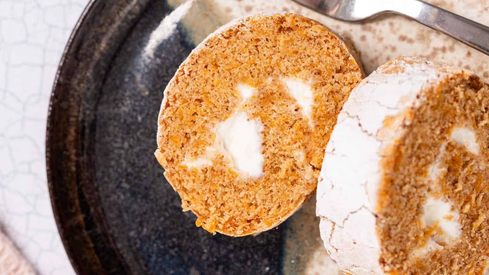 A close-up of two slices of rolled carrot cake with cream cheese filling, served on a ceramic plate with a fork nearby—a delicious twist perfect for fans of pumpkin dessert recipes.