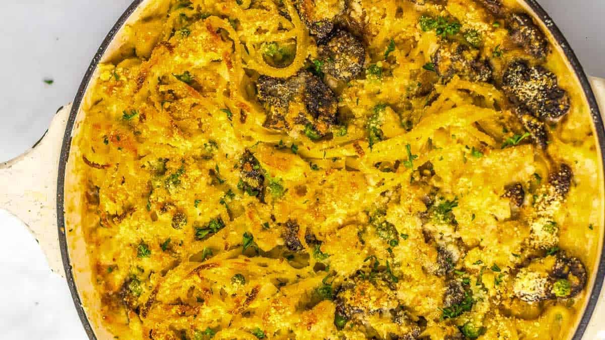 Baked spaghetti casserole with a golden, crispy cheese topping and visible mushrooms in a round, white dish.