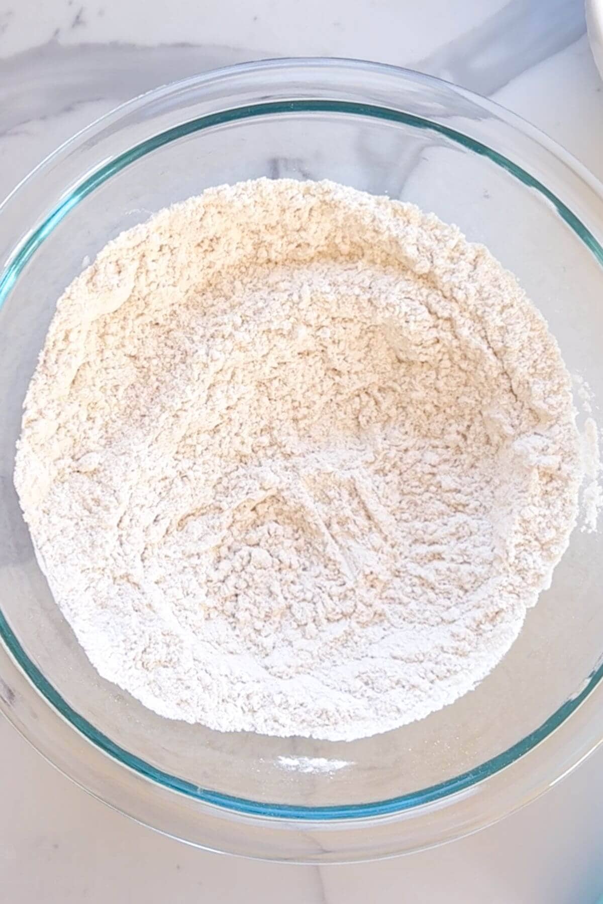 A glass bowl filled with flour sits on a white surface.