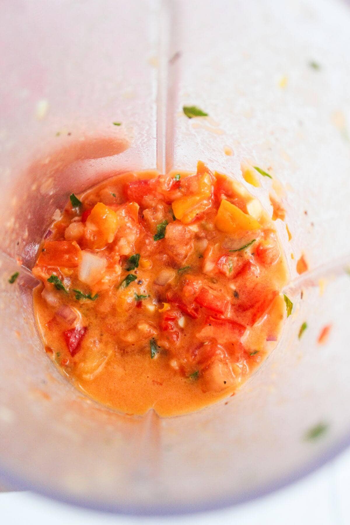 Chopped vegetables and liquid mixture inside a blender, blending into a chunky sauce or salsa.