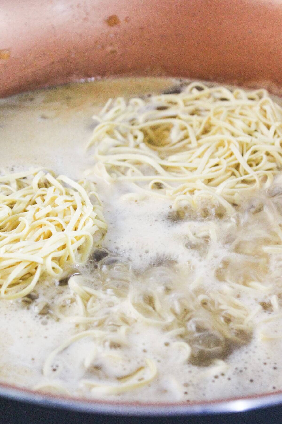 Uncooked noodles boiling in a pot of water.