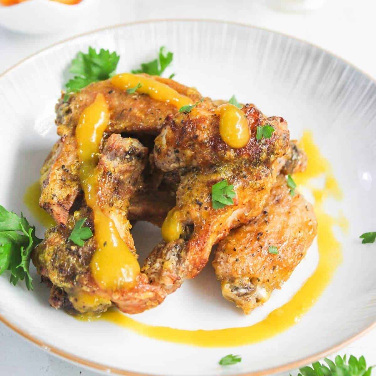 Three seasoned chicken wings topped with yellow sauce and garnished with parsley are served on a white plate.