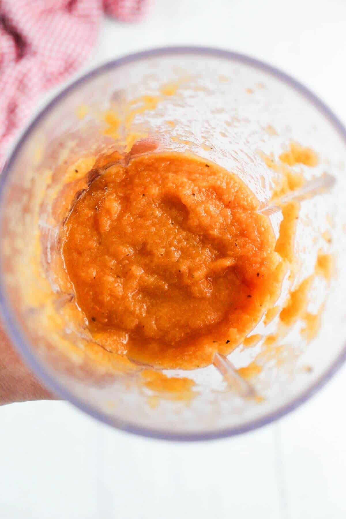 A blender cup filled with orange-colored pureed sauce or mixture, viewed from above.