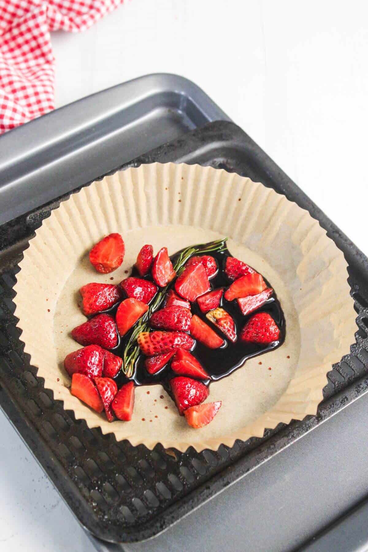 Chopped strawberries and a basil leaf with balsamic vinegar on parchment paper, placed on a baking tray, ready for roasting.
