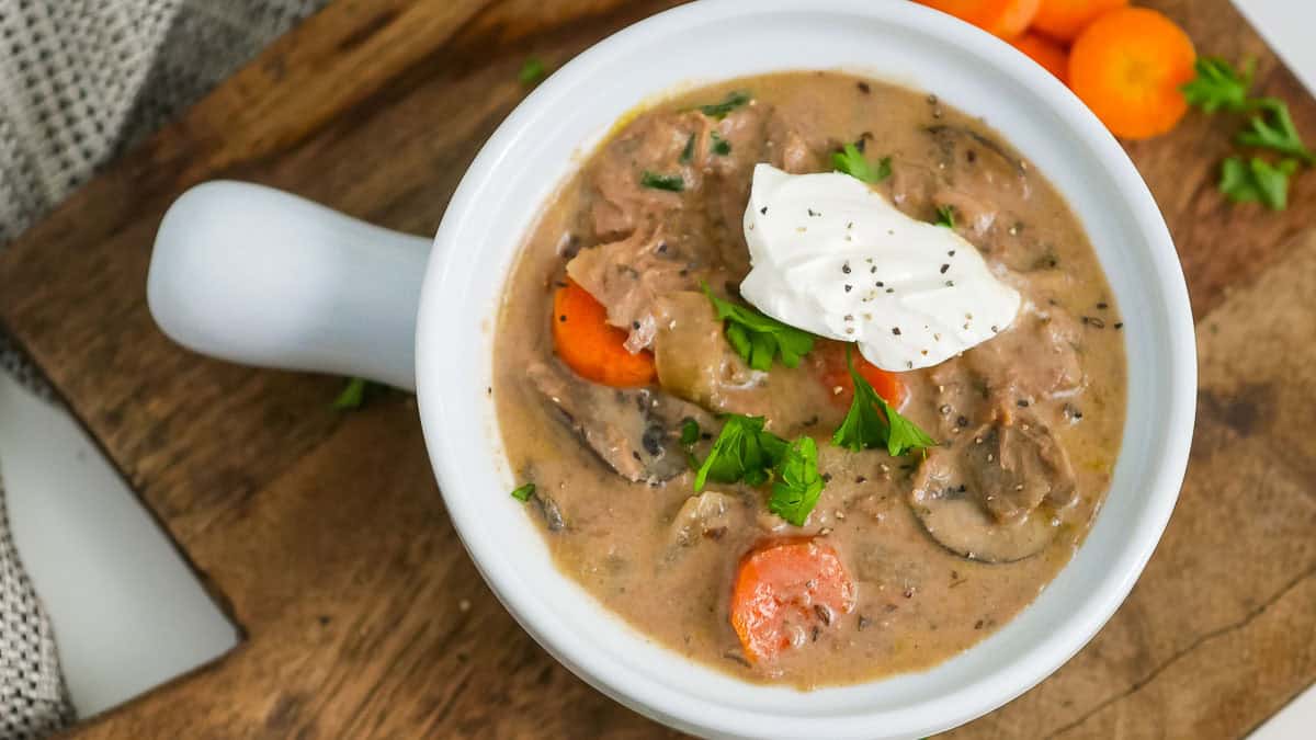 A bowl of creamy beef stew with carrots, mushrooms, and herbs, topped with a dollop of sour cream and a sprinkle of black pepper.