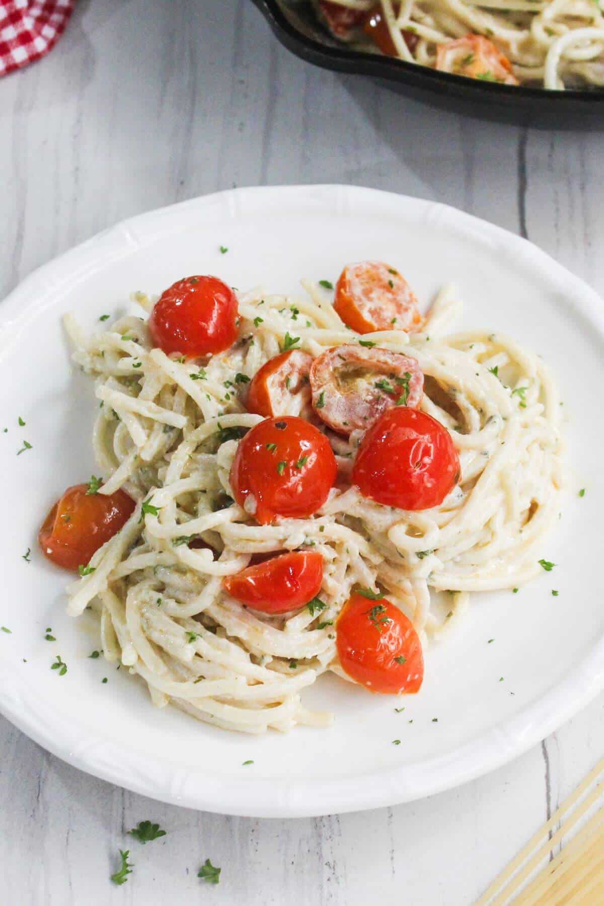 A plate of spaghetti with a creamy white sauce, cherry tomatoes, and chopped herbs, served on a white dish.
