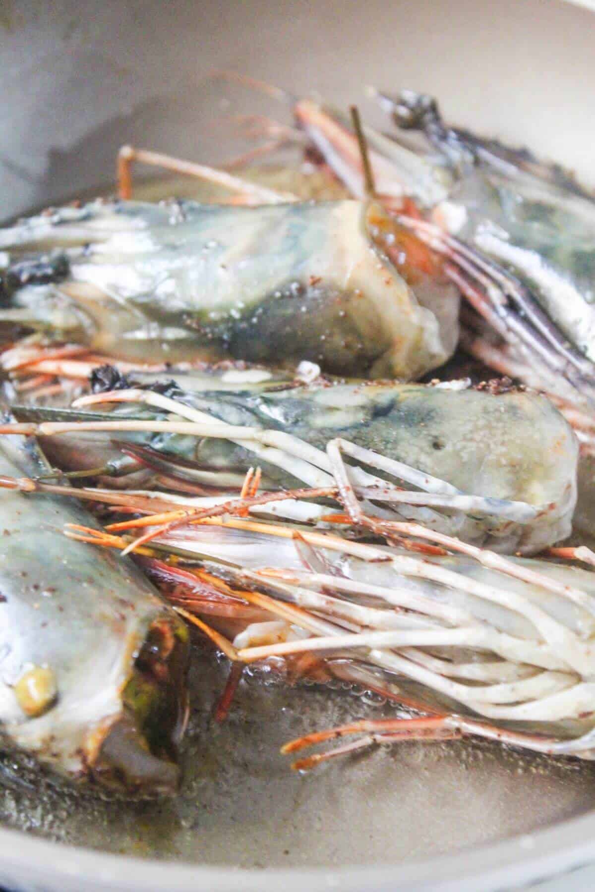 Several large prawn heads are being sautéed in oil in a pan.