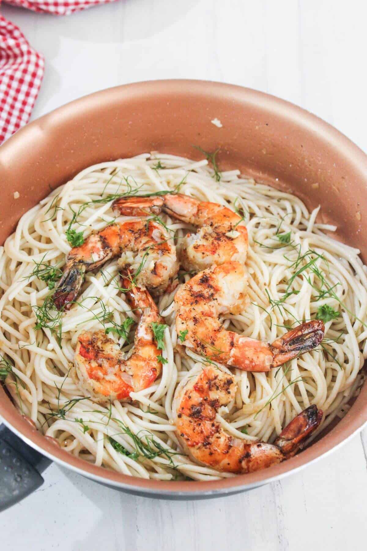 A pan filled with cooked spaghetti topped with grilled shrimp and garnished with fresh herbs.