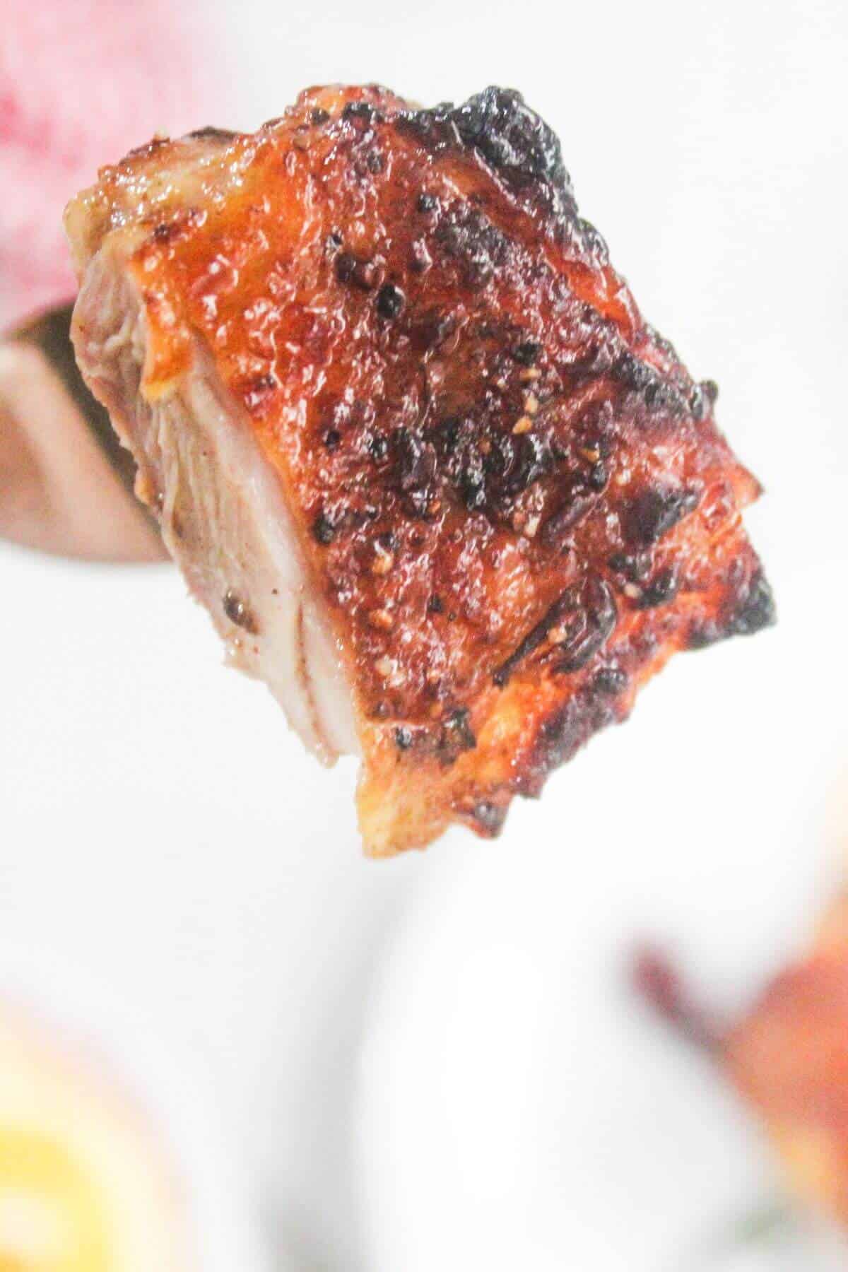 A close-up of a piece of cooked, crispy pork belly with browned and slightly charred skin.