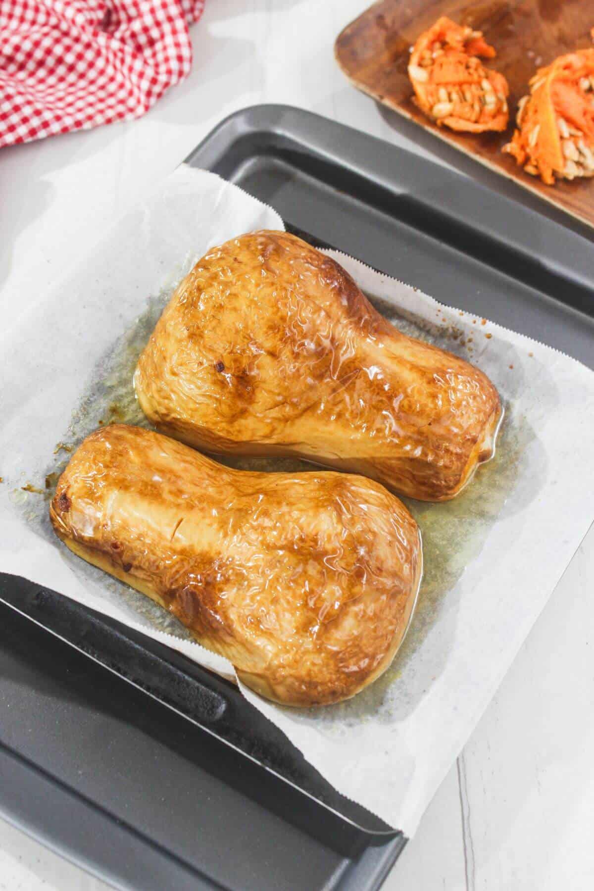 Two roasted butternut squash halves on a parchment-lined baking tray, with squash skins facing up.