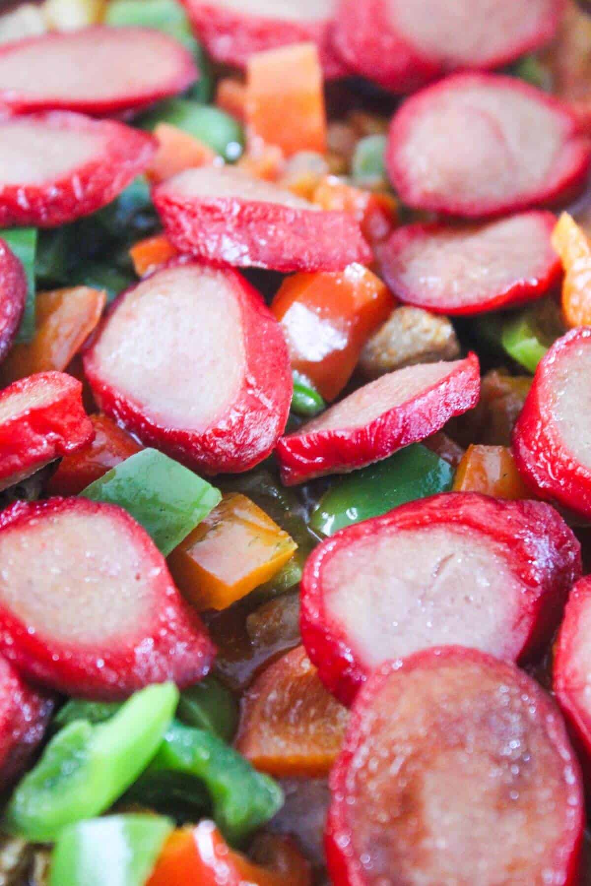 Sliced red sausage with chopped green and orange bell peppers, cooked together in a pan.