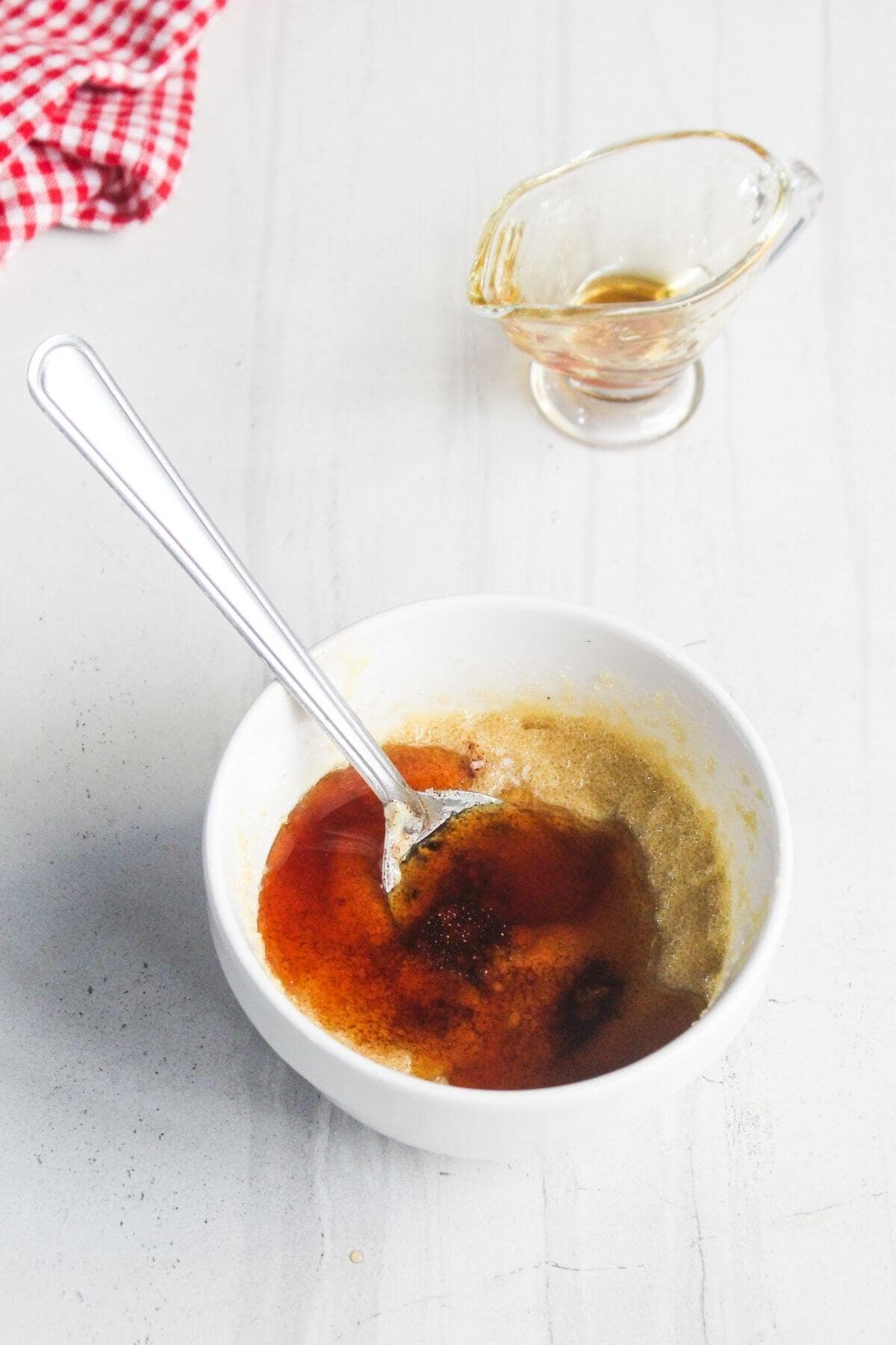 A white bowl with brown liquid and a spoon inside, next to a small glass container with additional liquid, on a white countertop.