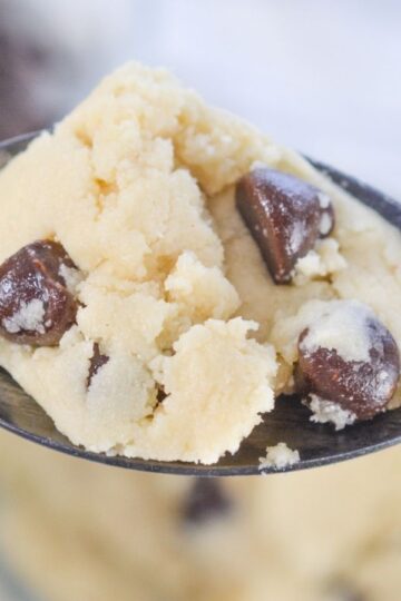A close-up of a spoon holding a scoop of chocolate chip cookie dough, with chocolate chips visible throughout.