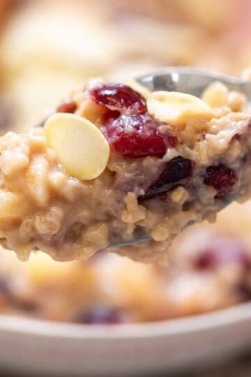 A close-up of a spoonful of oatmeal with dried cranberries, almond slices, and pieces of fruit.