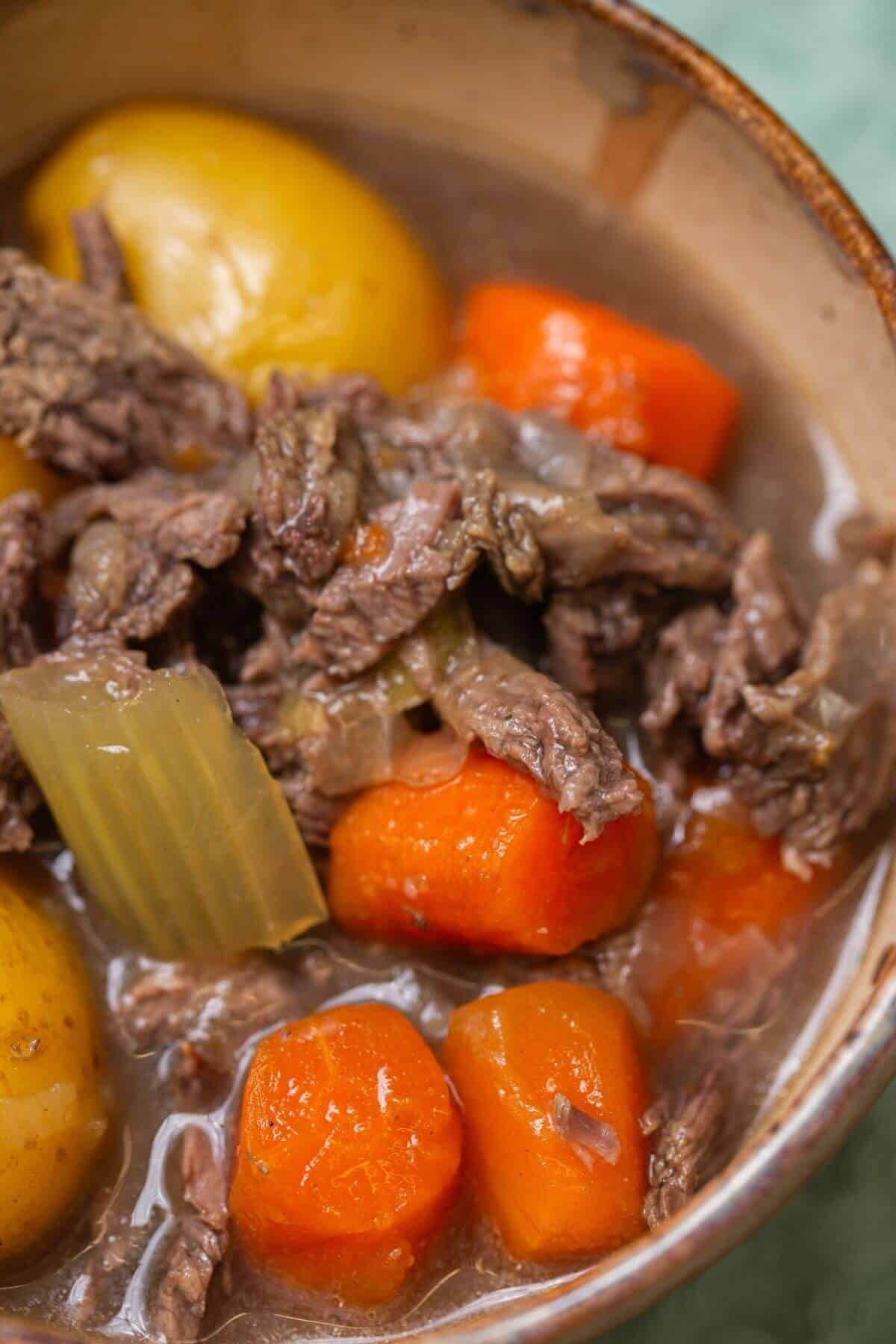 A bowl of beef stew with chunks of beef, carrots, potatoes, and celery in a broth.