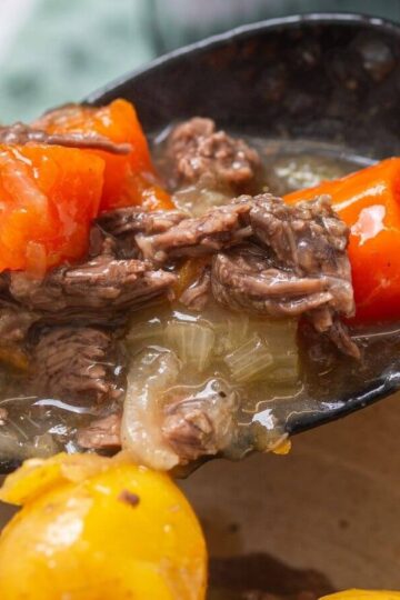 A ladle serves beef stew with shredded beef, carrots, onions, and potatoes into a bowl.