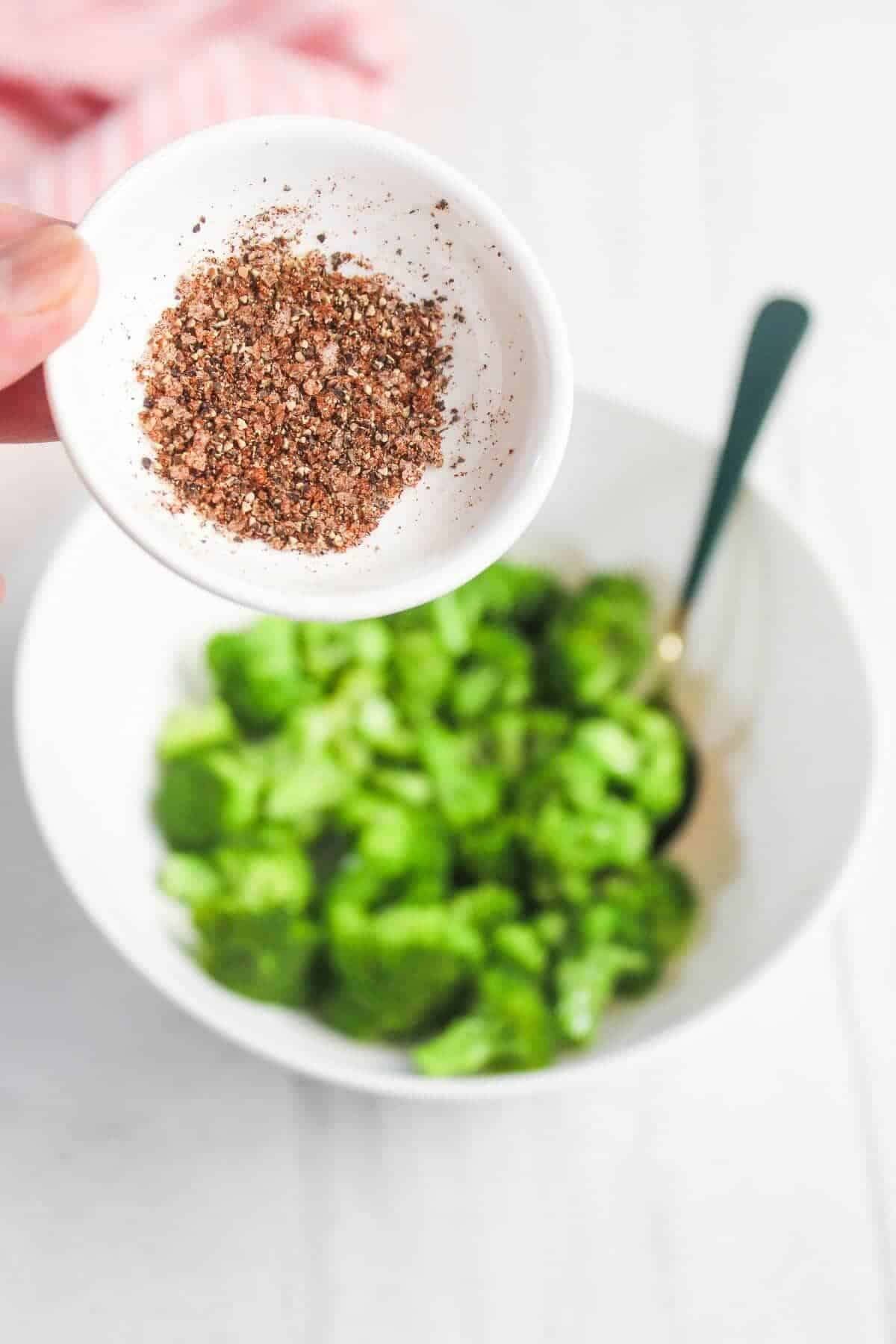 A small white dish containing a spice mix is held above a bowl of chopped green lettuce with a fork inside.