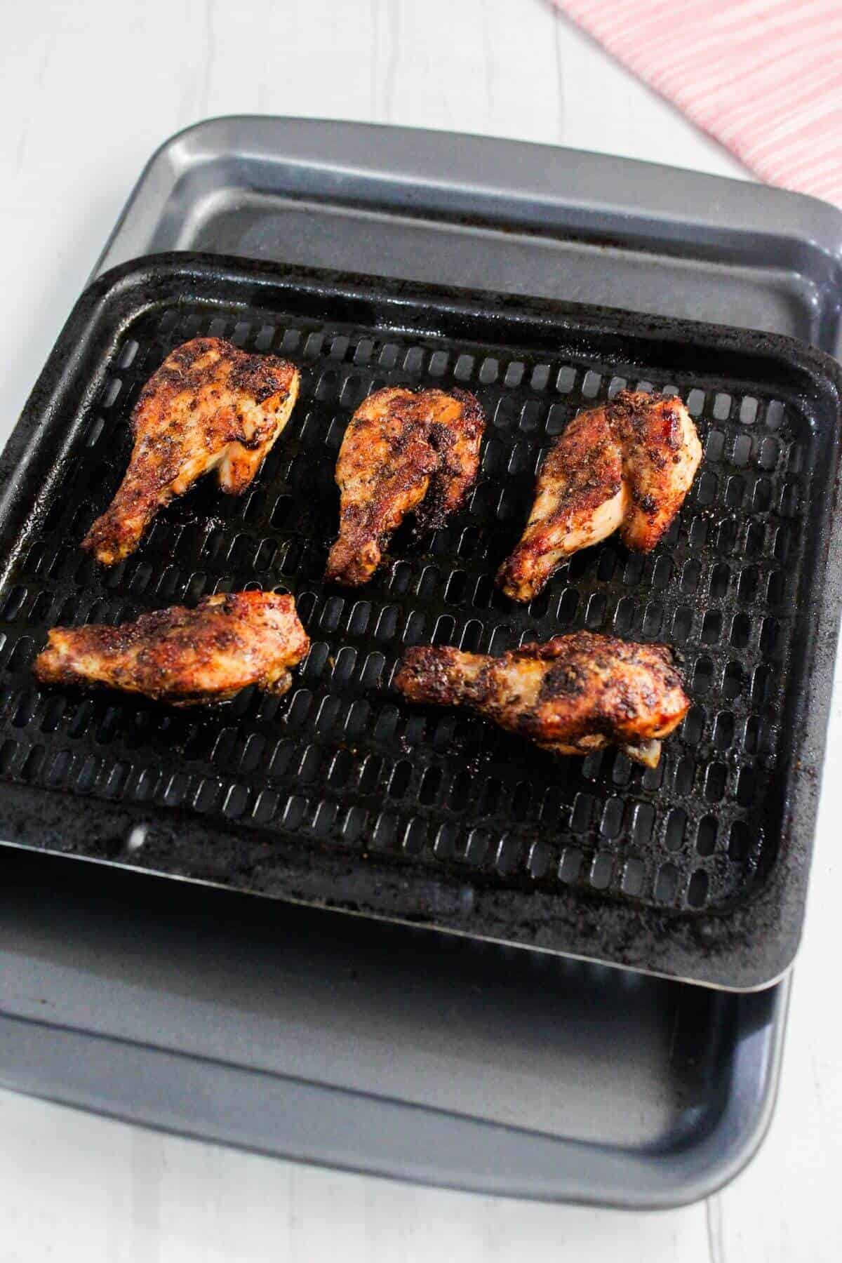 Five seasoned chicken wings on a black grill tray, placed over a metal baking sheet on a light-colored surface.