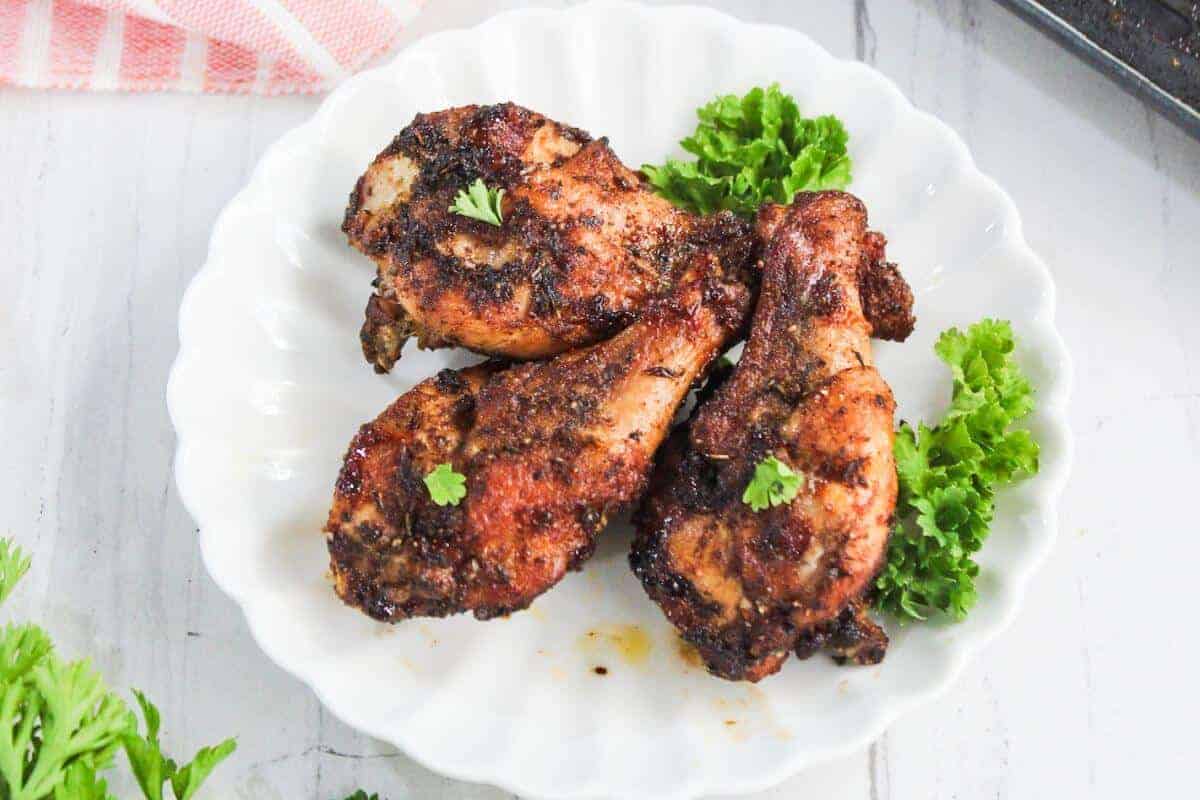 Three pieces of seasoned, grilled chicken are arranged on a white plate with sprigs of parsley as garnish.