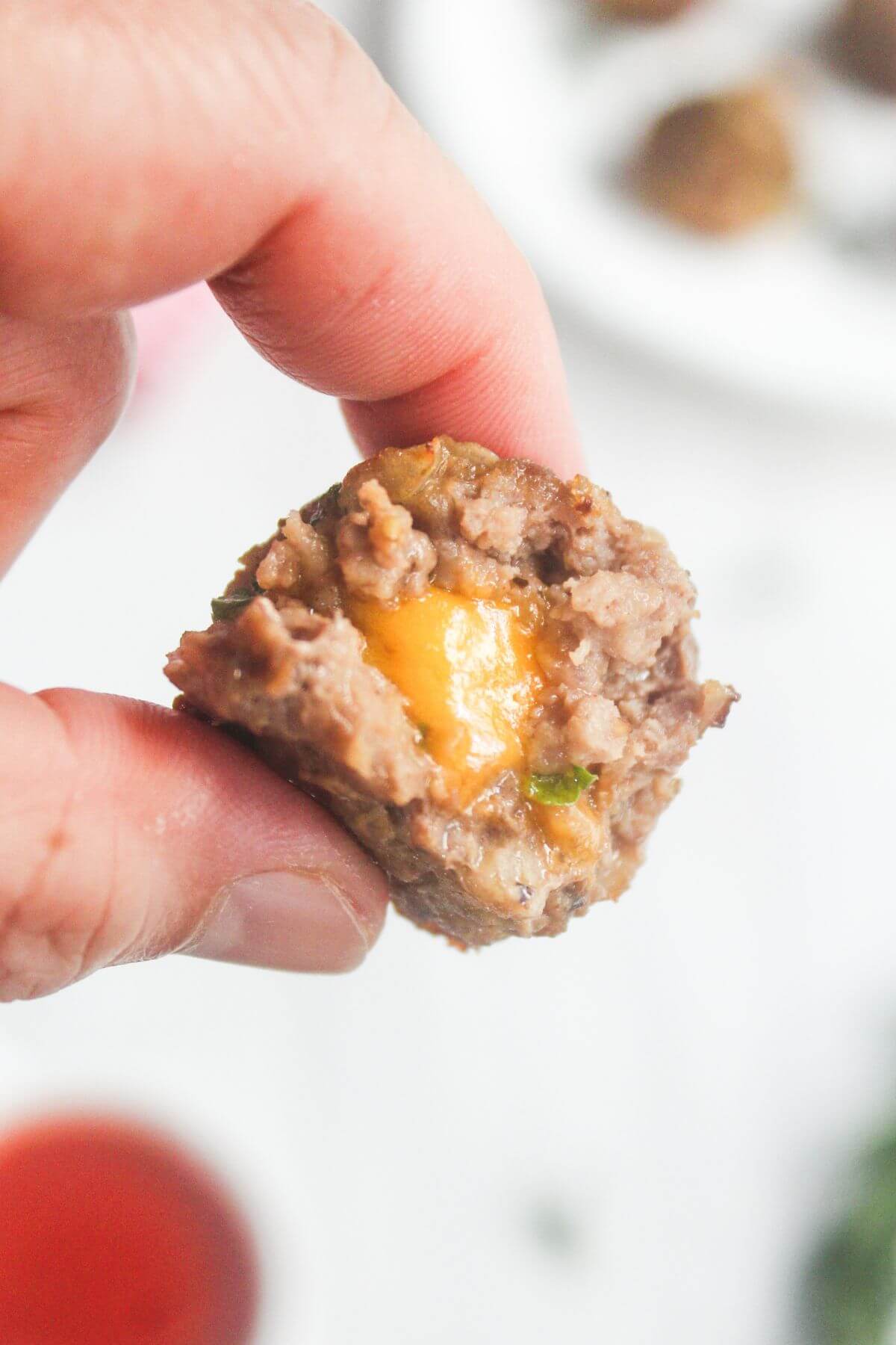 A hand holding a half-eaten meatball with melted cheese and green herbs visible inside.