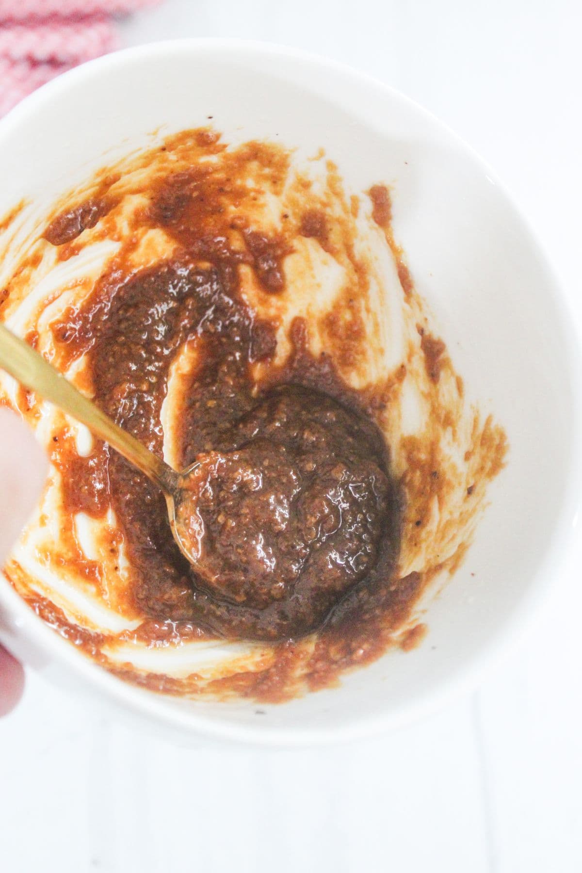A white bowl containing a thick, brown mixture being stirred with a gold spoon.