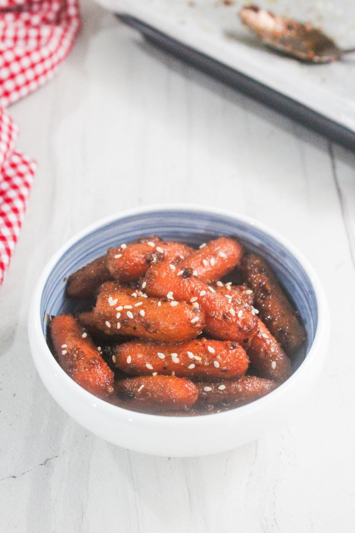 A bowl of glazed Korean rice cakes garnished with sesame seeds on a white surface.