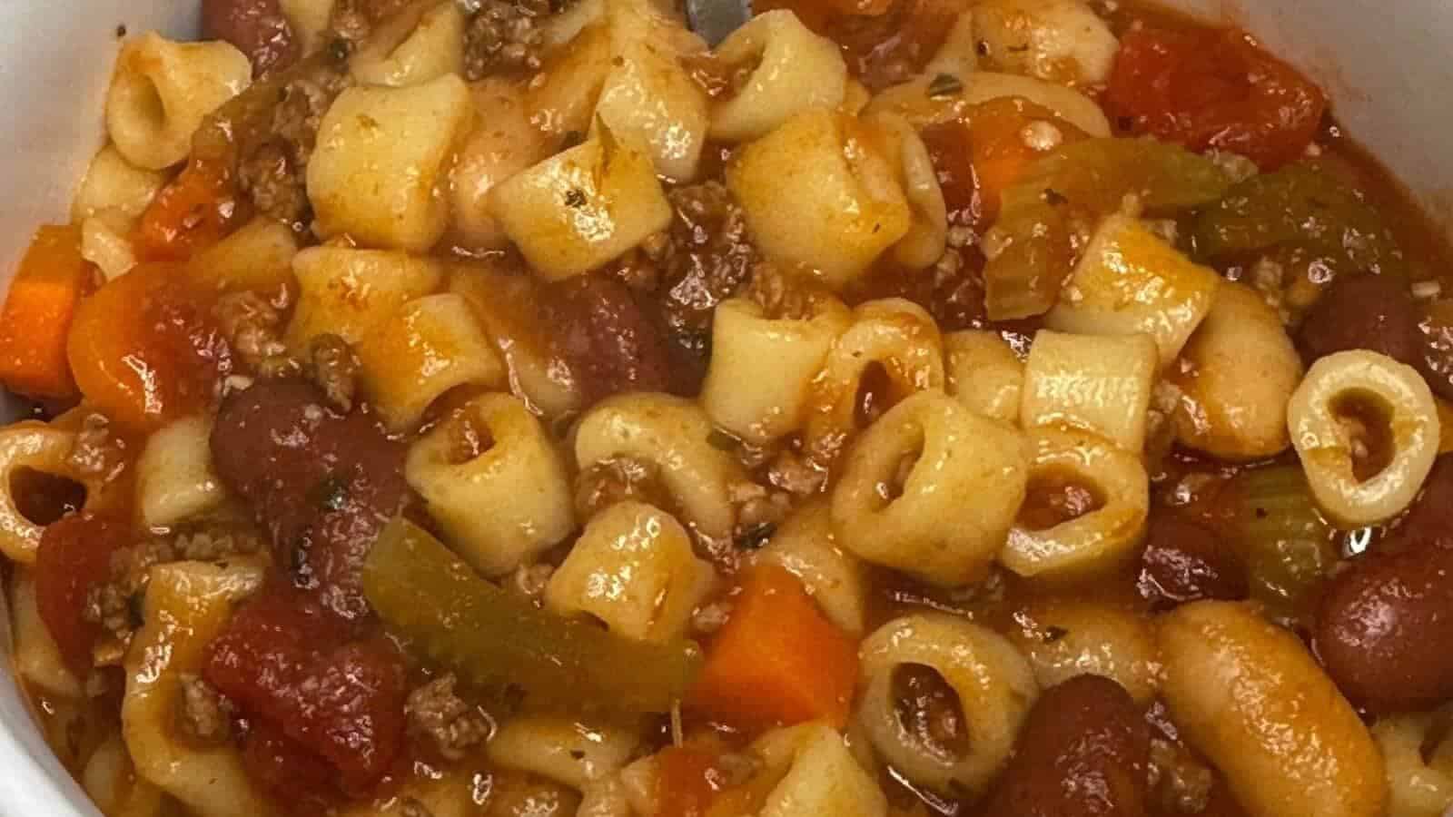 A bowl of pasta e fagioli soup with ditalini pasta, kidney beans, ground meat, tomatoes, carrots, and celery in a tomato-based broth.
