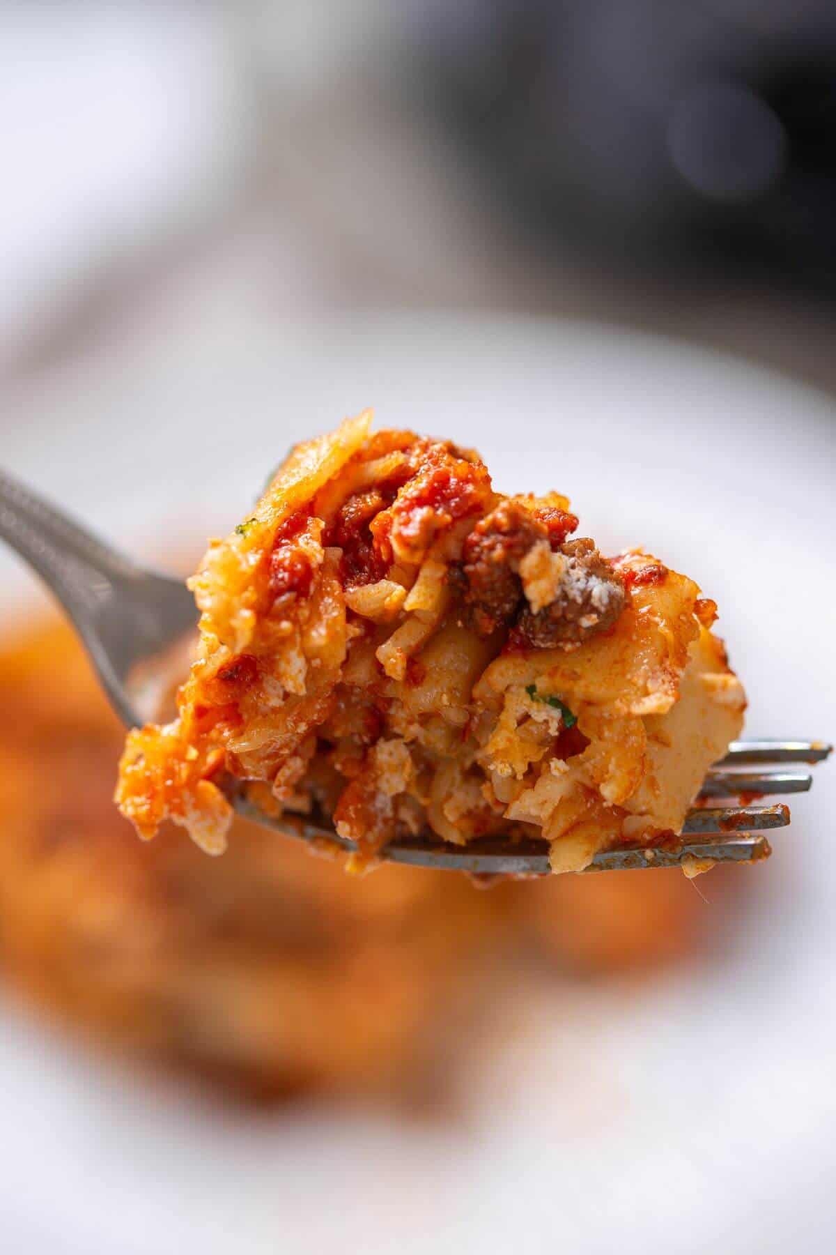 A close-up of a fork holding a bite of lasagna, showing layers of pasta, meat sauce, and melted cheese.