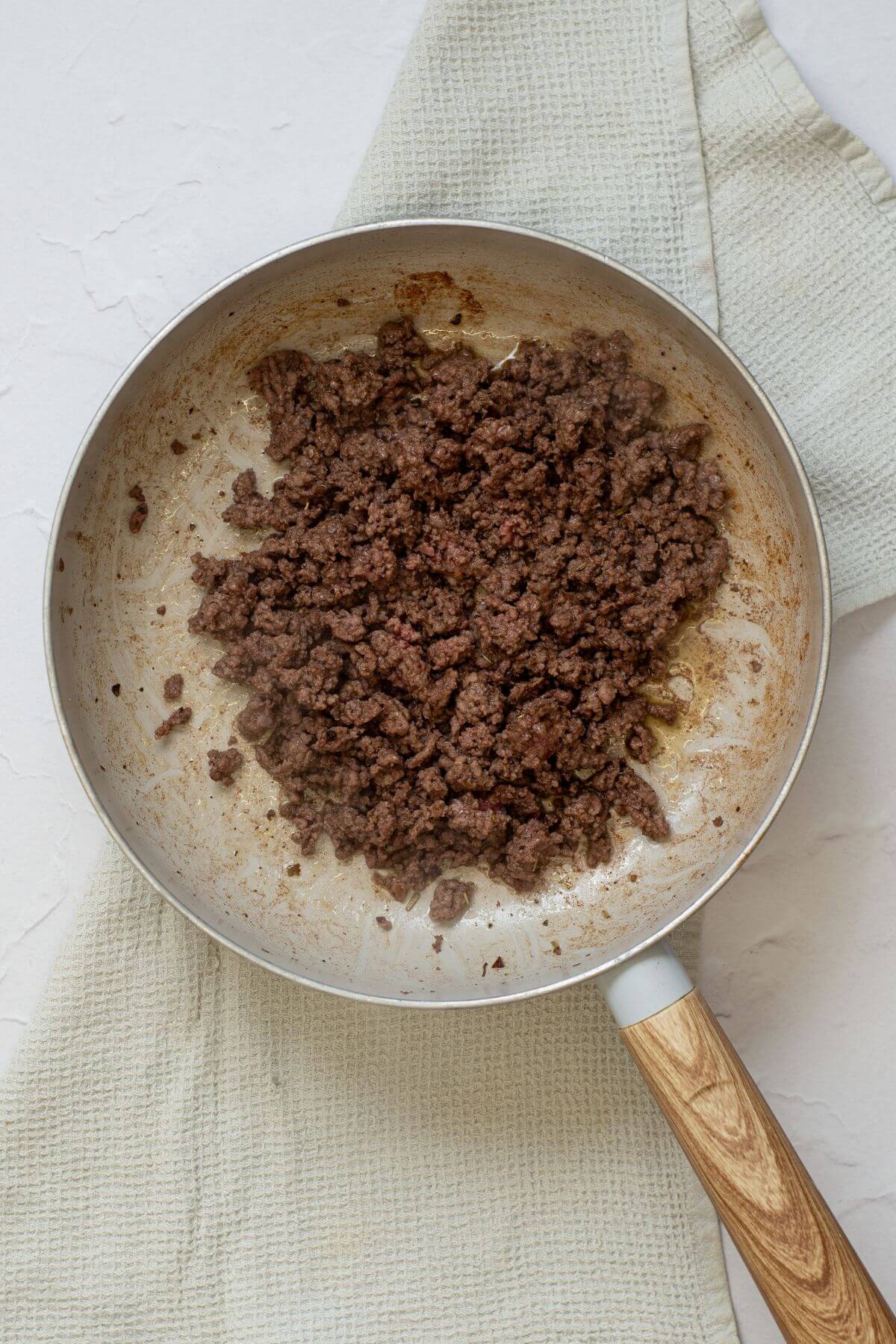 Cooked ground beef in a skillet resting on a textured light green kitchen towel.