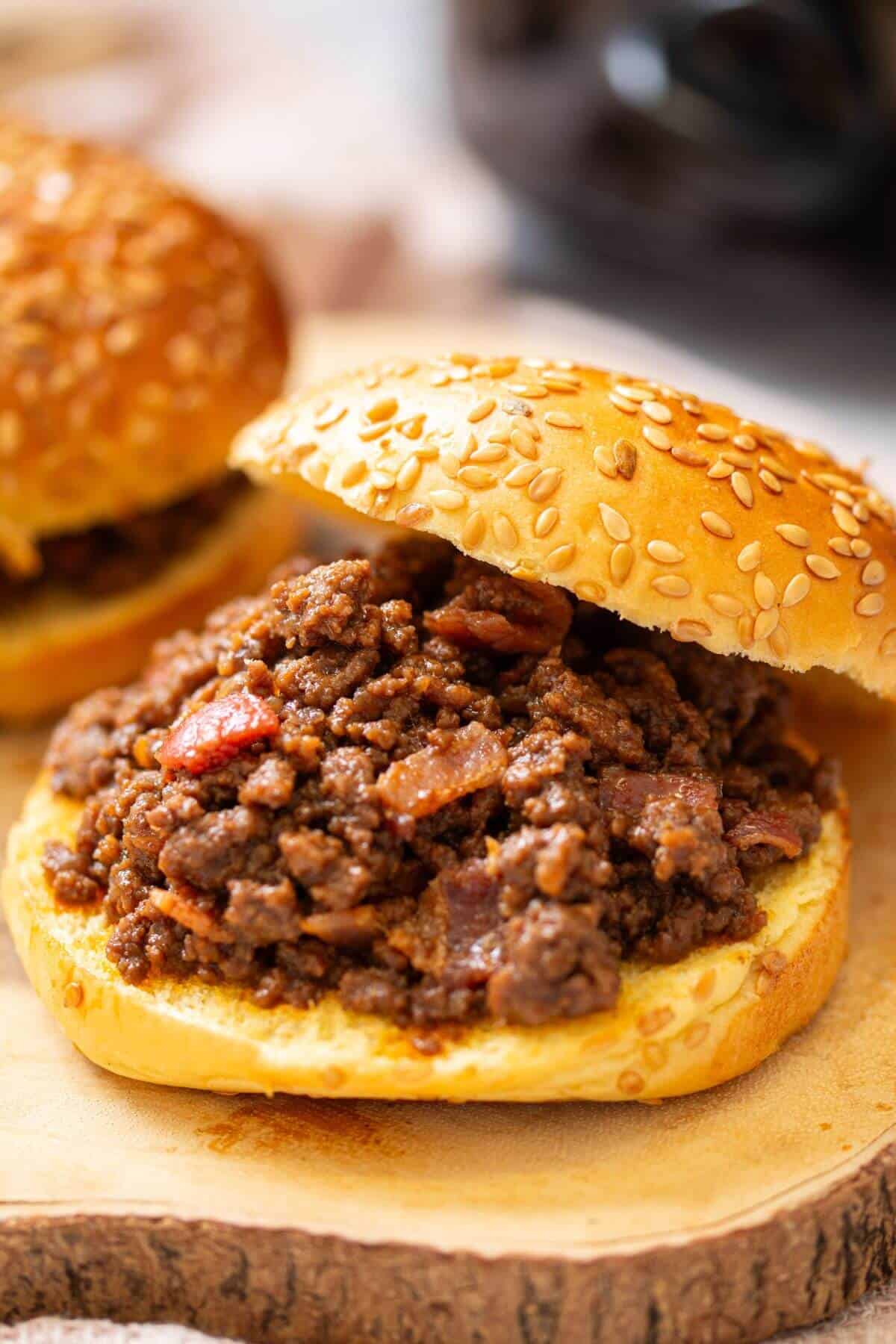 A sesame seed hamburger bun filled with seasoned ground beef and diced tomatoes, served open-faced on a wooden surface.
