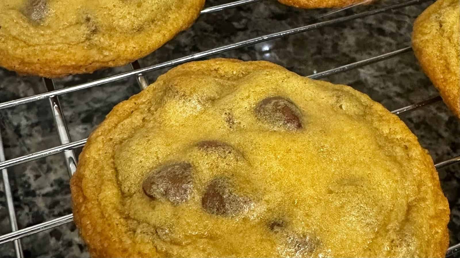 A chocolate chip cookie cooling on a wire rack, with other cookies partially visible, set on a granite countertop.
