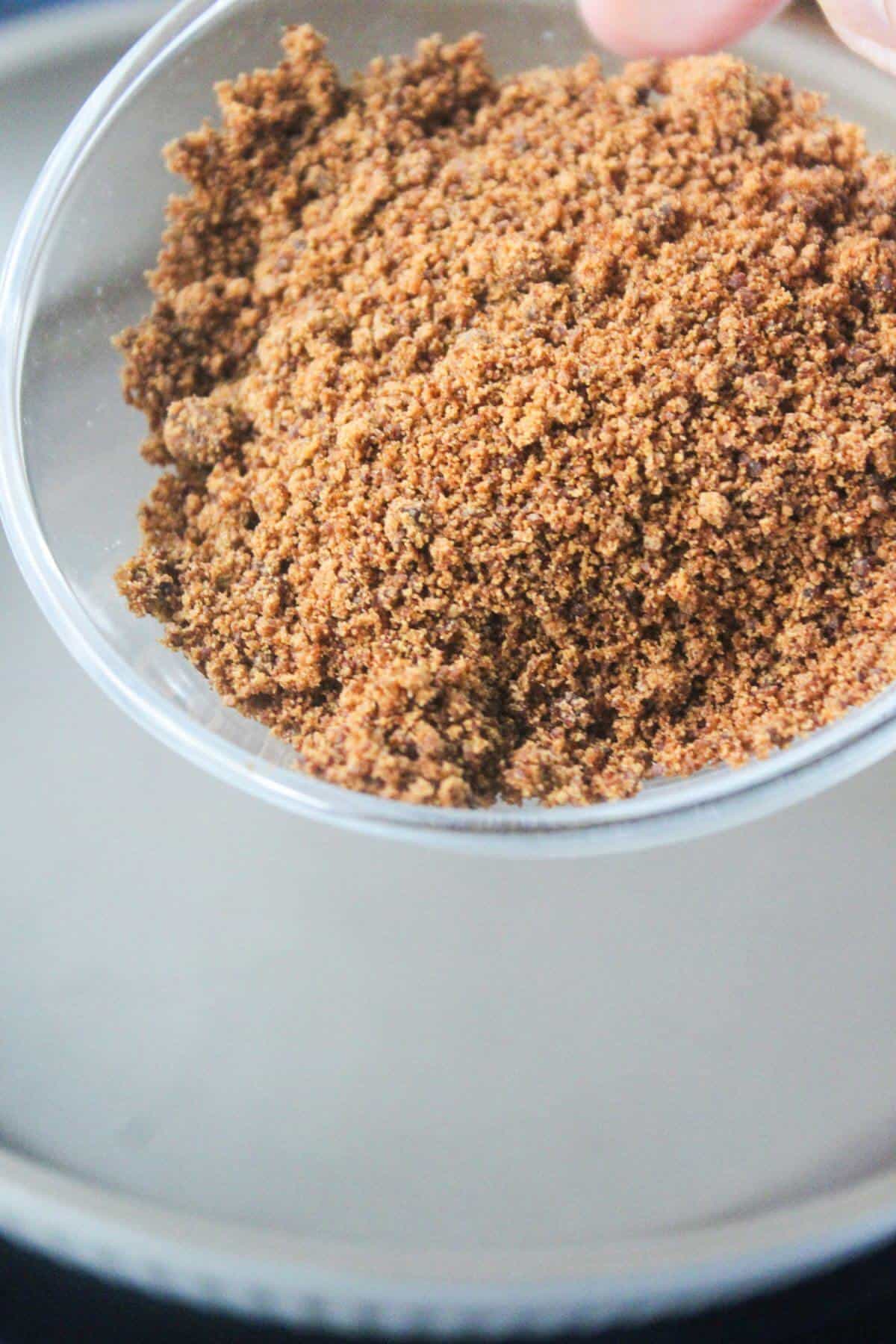 A clear bowl filled with light brown granulated sugar held above a gray surface.