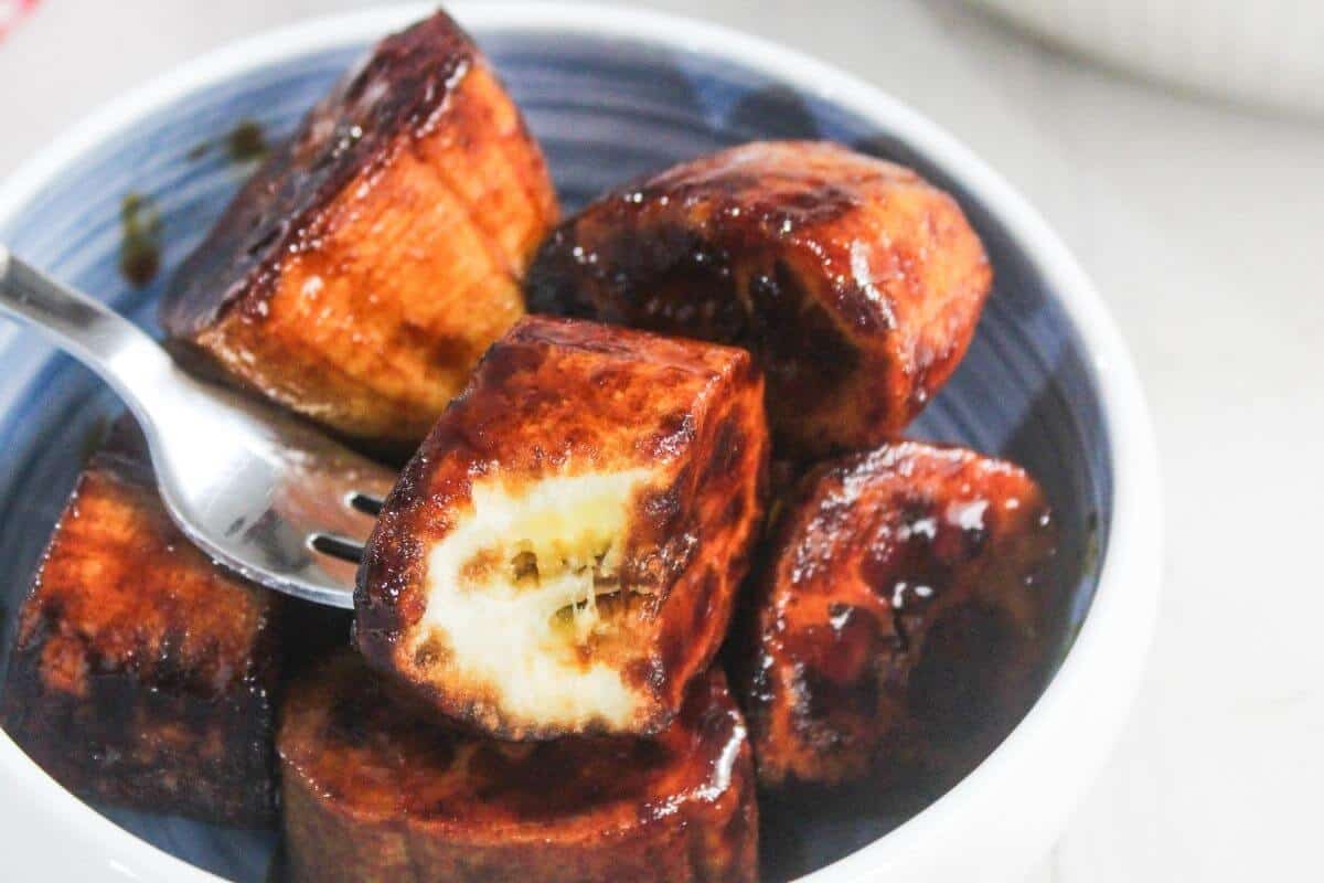 A bowl of caramelized, sliced plantains with a fork holding a piece that has a bite taken out of it.