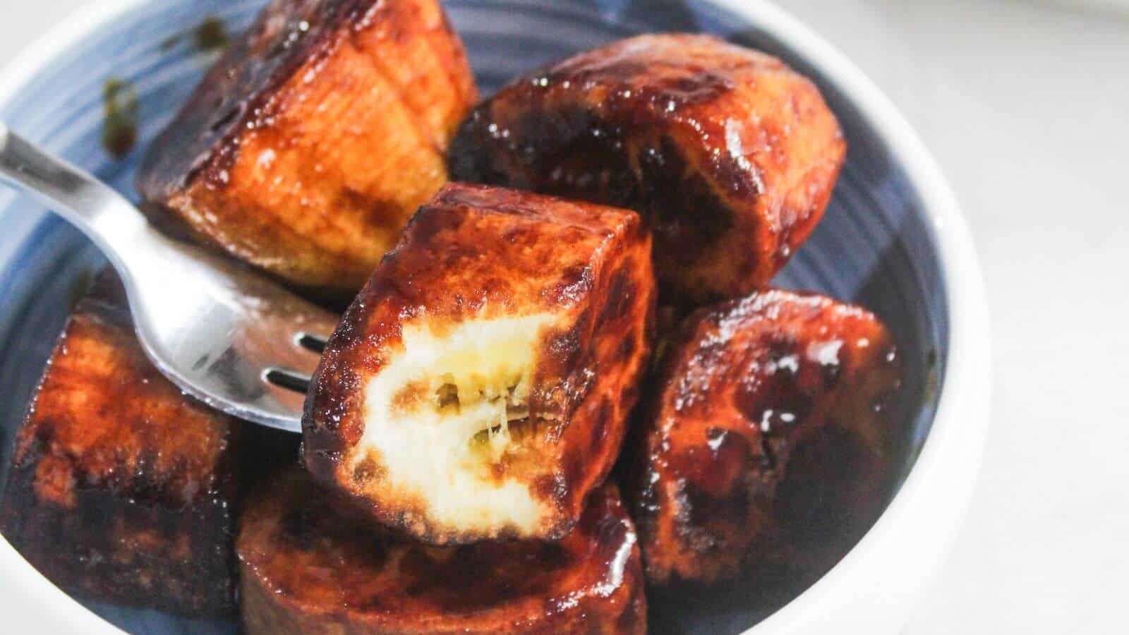 A bowl of caramelized fried plantains with a fork holding one piece, showing the inside of the plantain.
