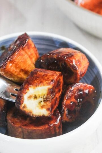 A bowl of caramelized plantain slices with a fork picking up one piece showing the soft inside.