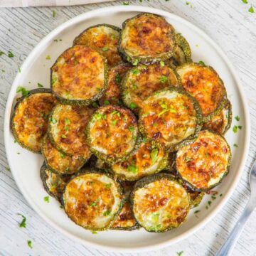 A plate of baked zucchini slices topped with melted cheese and herbs, served on a white dish.