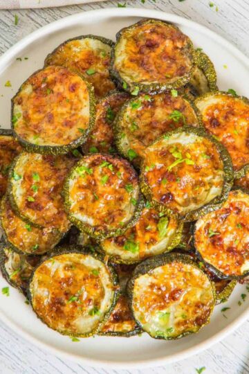 A plate of baked zucchini slices topped with melted cheese and herbs, served on a white dish.