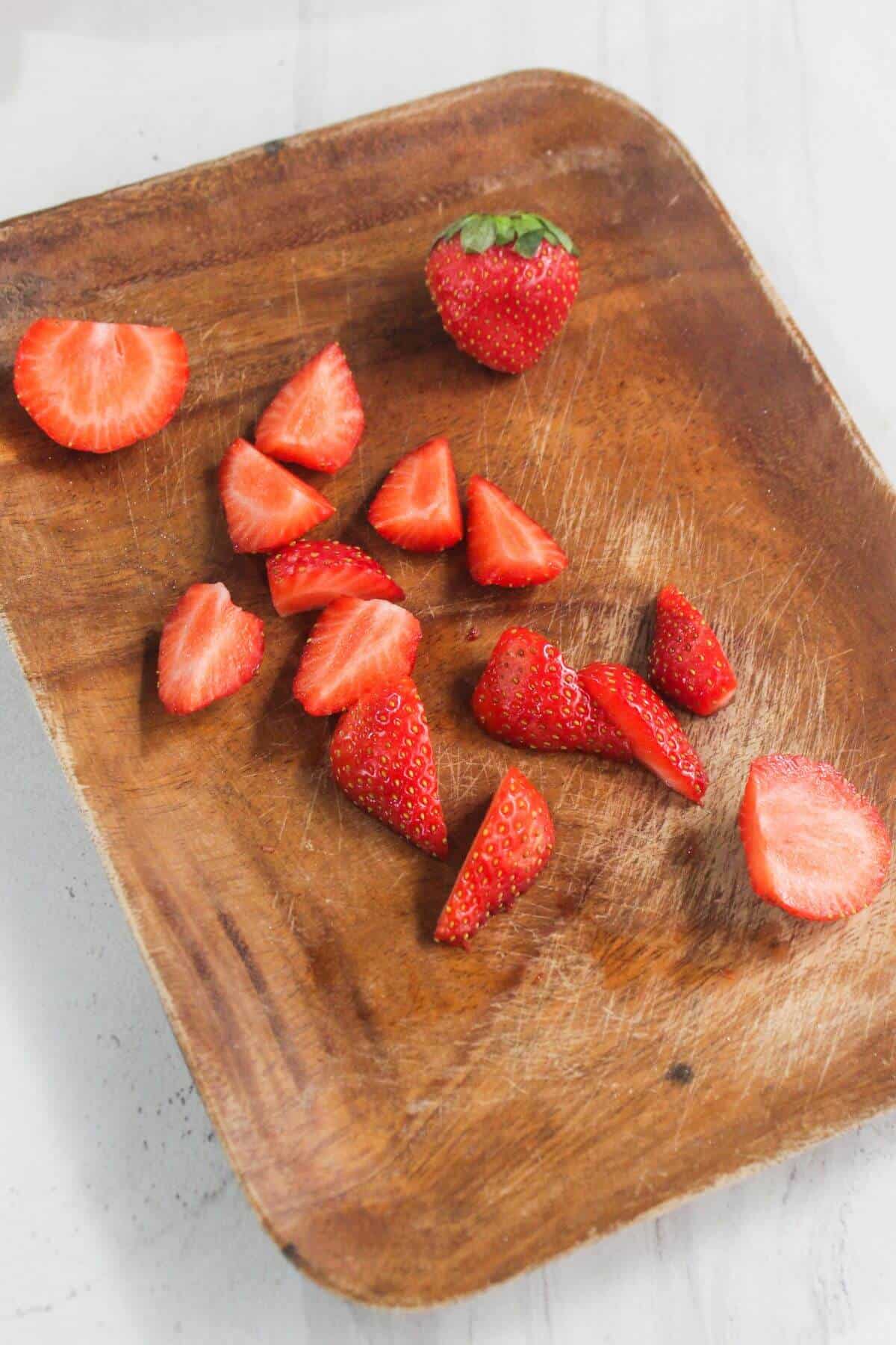 A whole strawberry and several sliced strawberry pieces are arranged on a scratched wooden cutting board.