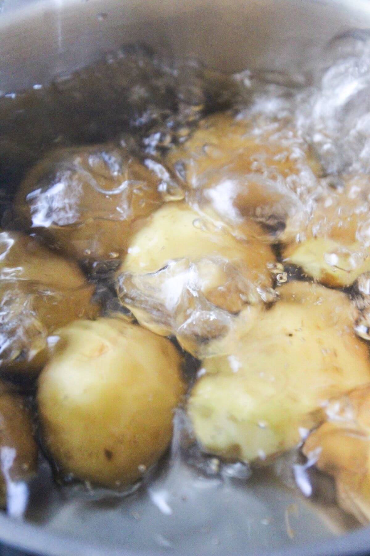 Several whole potatoes are boiling in a pot of water, with bubbles visible on the surface.