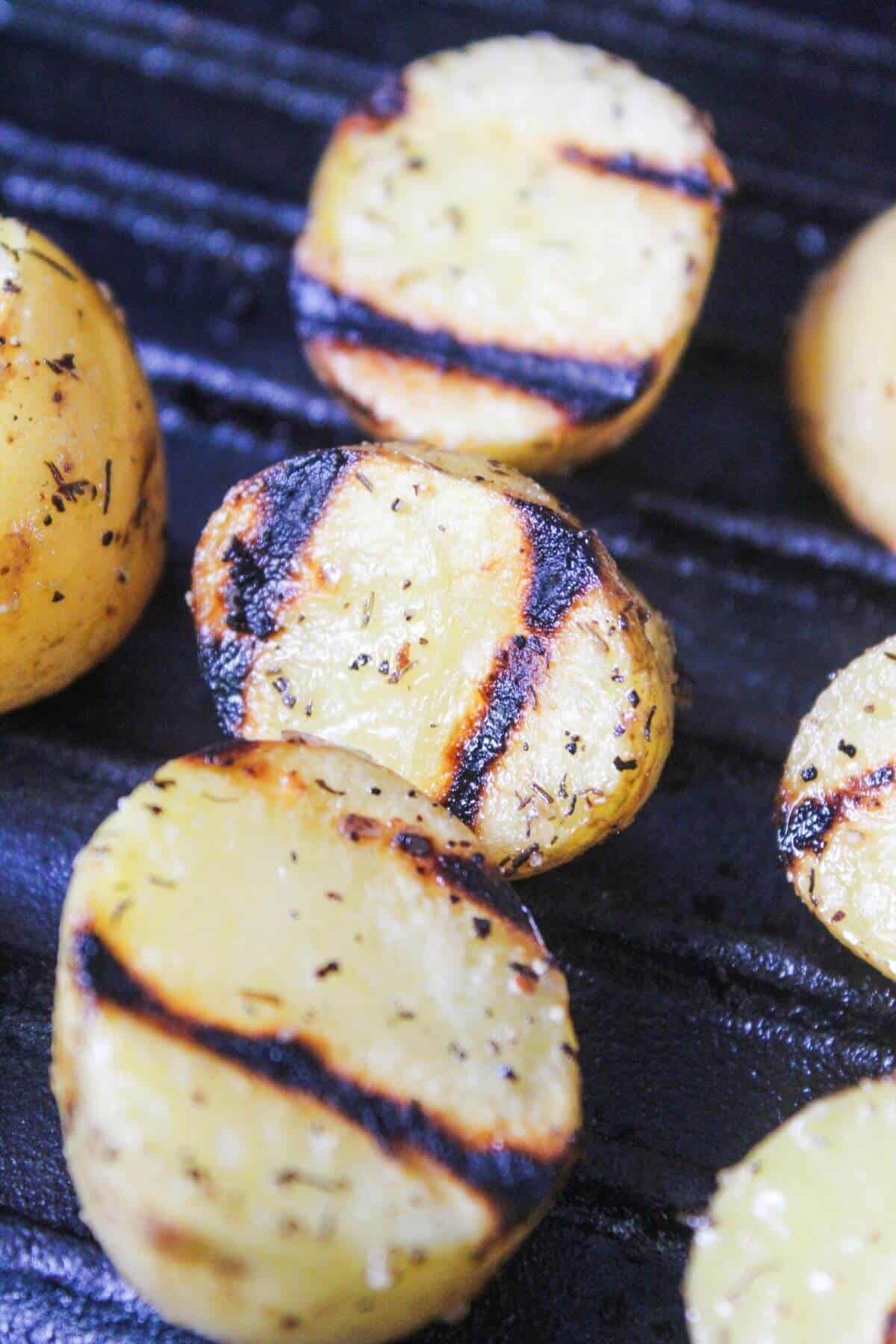 Sliced potatoes with seasoning grill marks are shown cooking on a black grill surface.