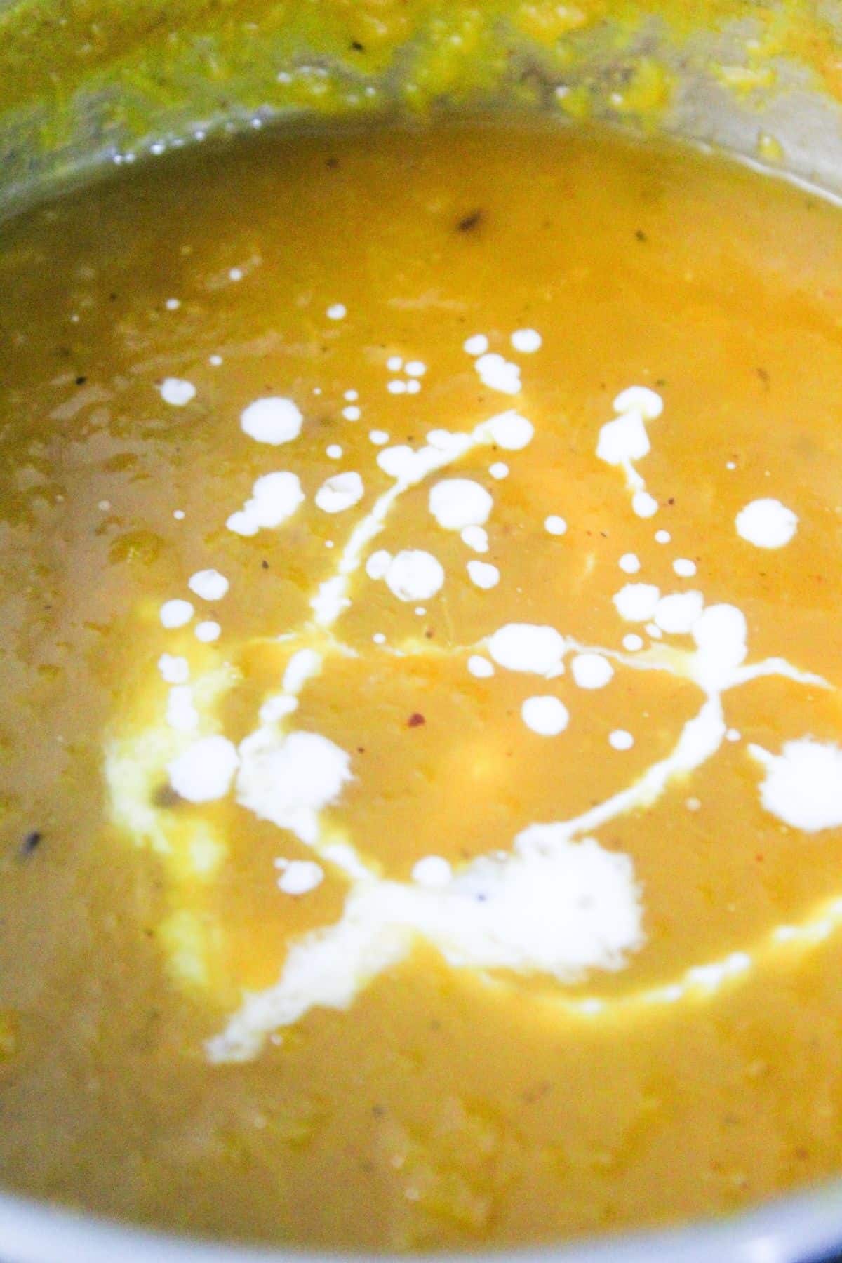 A close-up of a pot filled with yellow soup, garnished with a swirl of white cream on the surface.