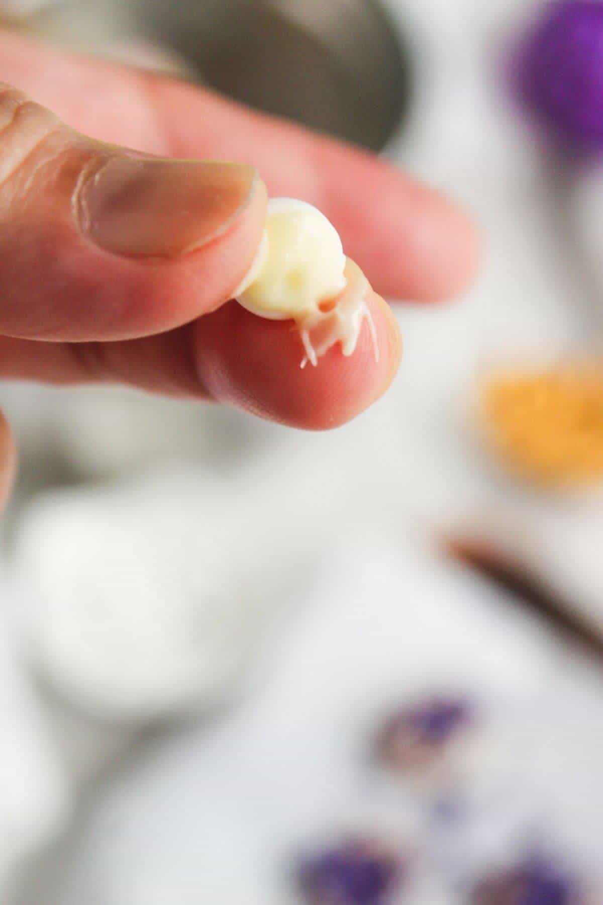 A close-up of a hand holding a small, white candy skull with visible details. Blurred background with various objects out of focus.